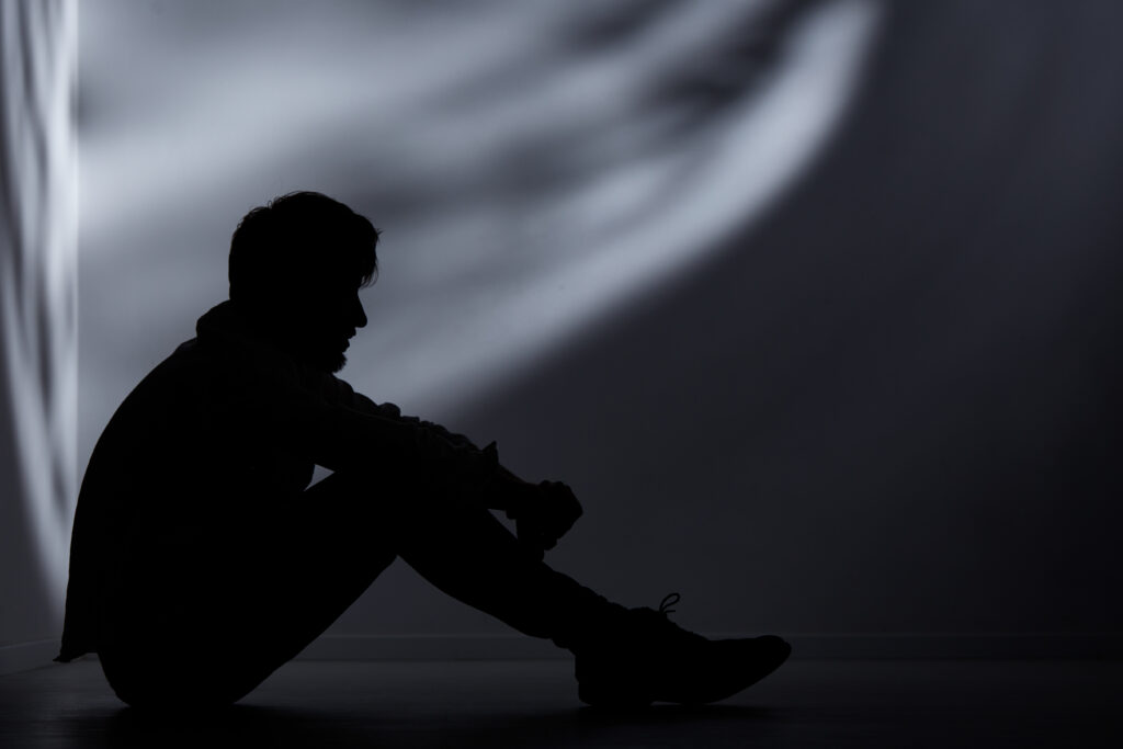 Mann sitzt im dunklen Raum am Boden und ist depressiv.