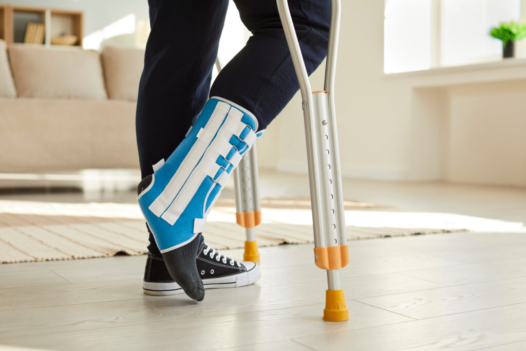 Leg of man walking with crutches in ankle brace with support adjustable strap fracture fixator.