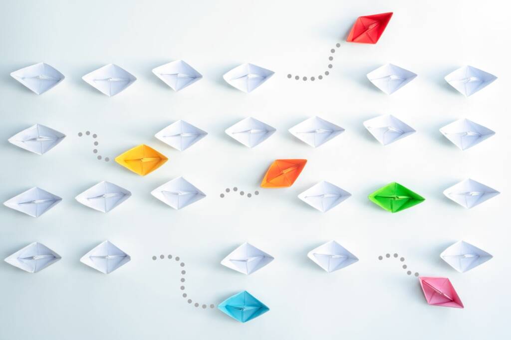 Weiße und bunte Papierboote auf hellem Hintergrund, verbunden durch gepunktete Linien als Kommunikationsnetzwerk.