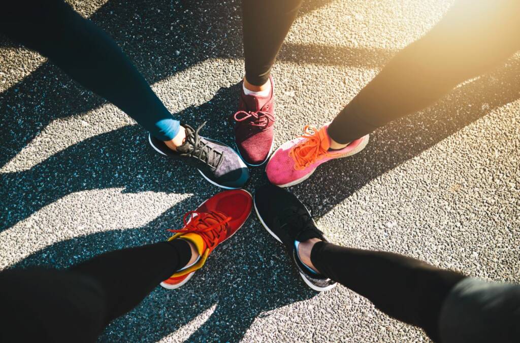 Vier Paar bunte Laufschuhe bilden einen Kreis auf Asphalt mit Sonnenlicht und Schatten.